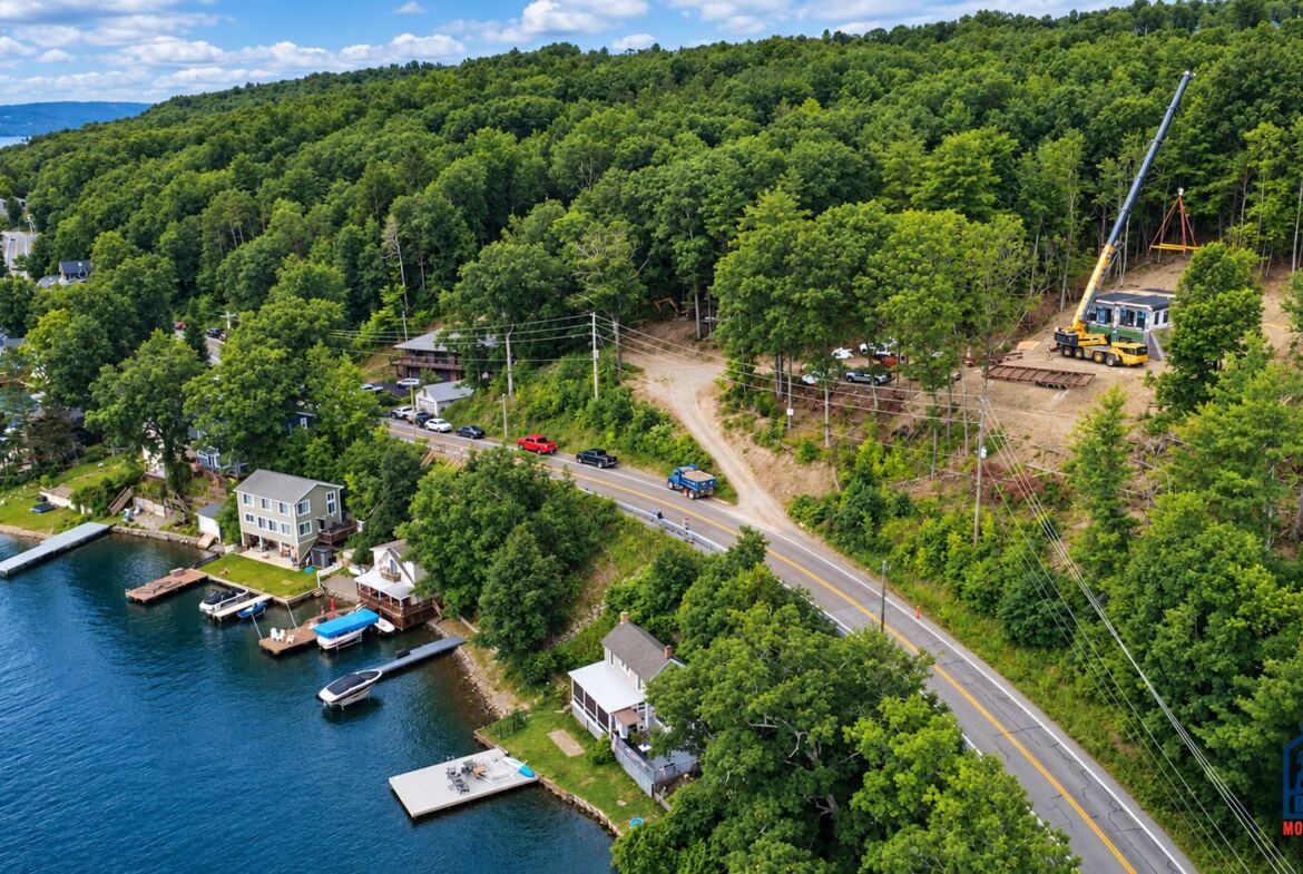 Aerial view of a modular home being set by crane on a lakeside lot